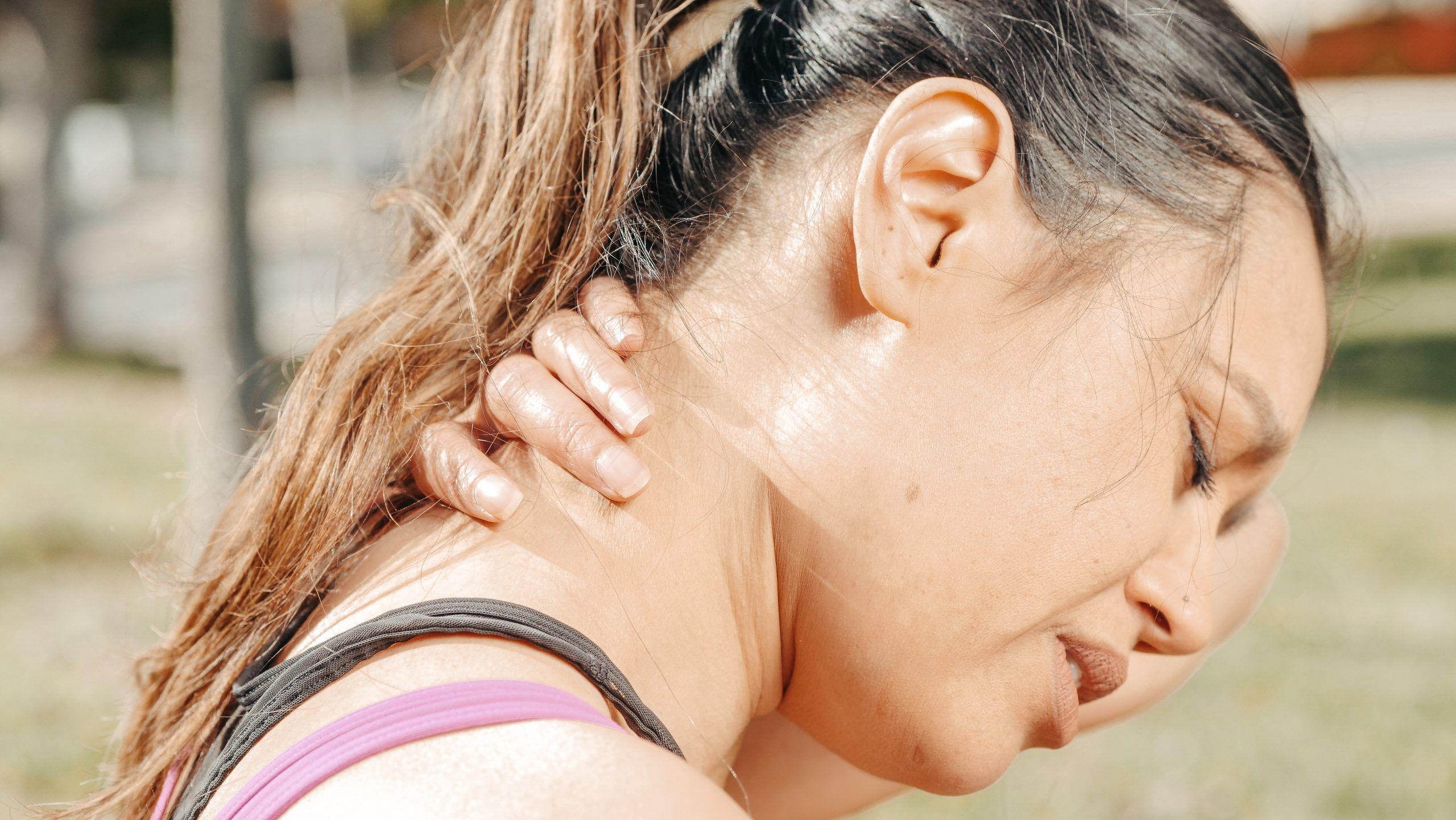 Woman grasping her neck in pain or discomfort outdoors.