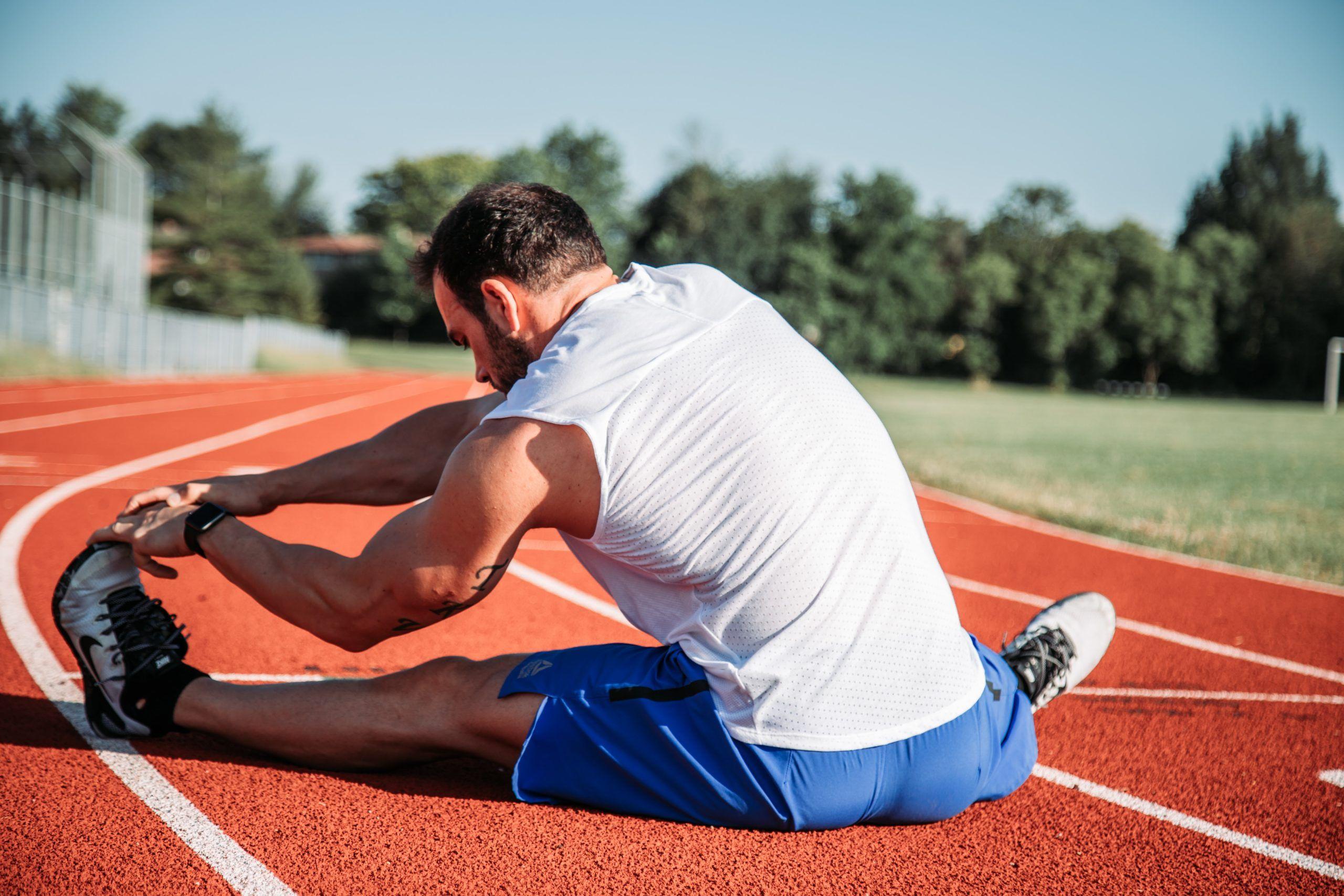 Man stretching on a red running track outdoors.