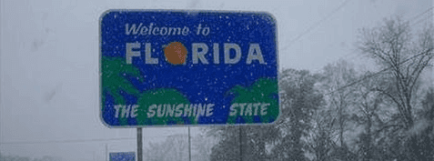 Sign reading 'Welcome to Florida, The Sunshine State' covered in snowflakes during a snowfall.