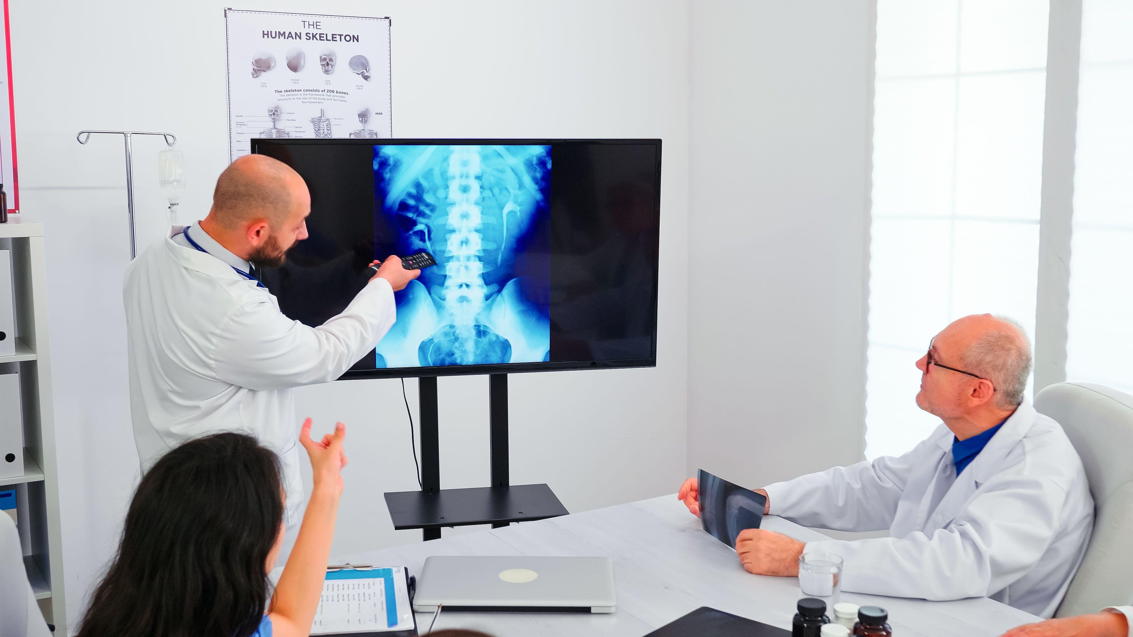 Experts discussing spine X-ray with colleagues in a medical office.