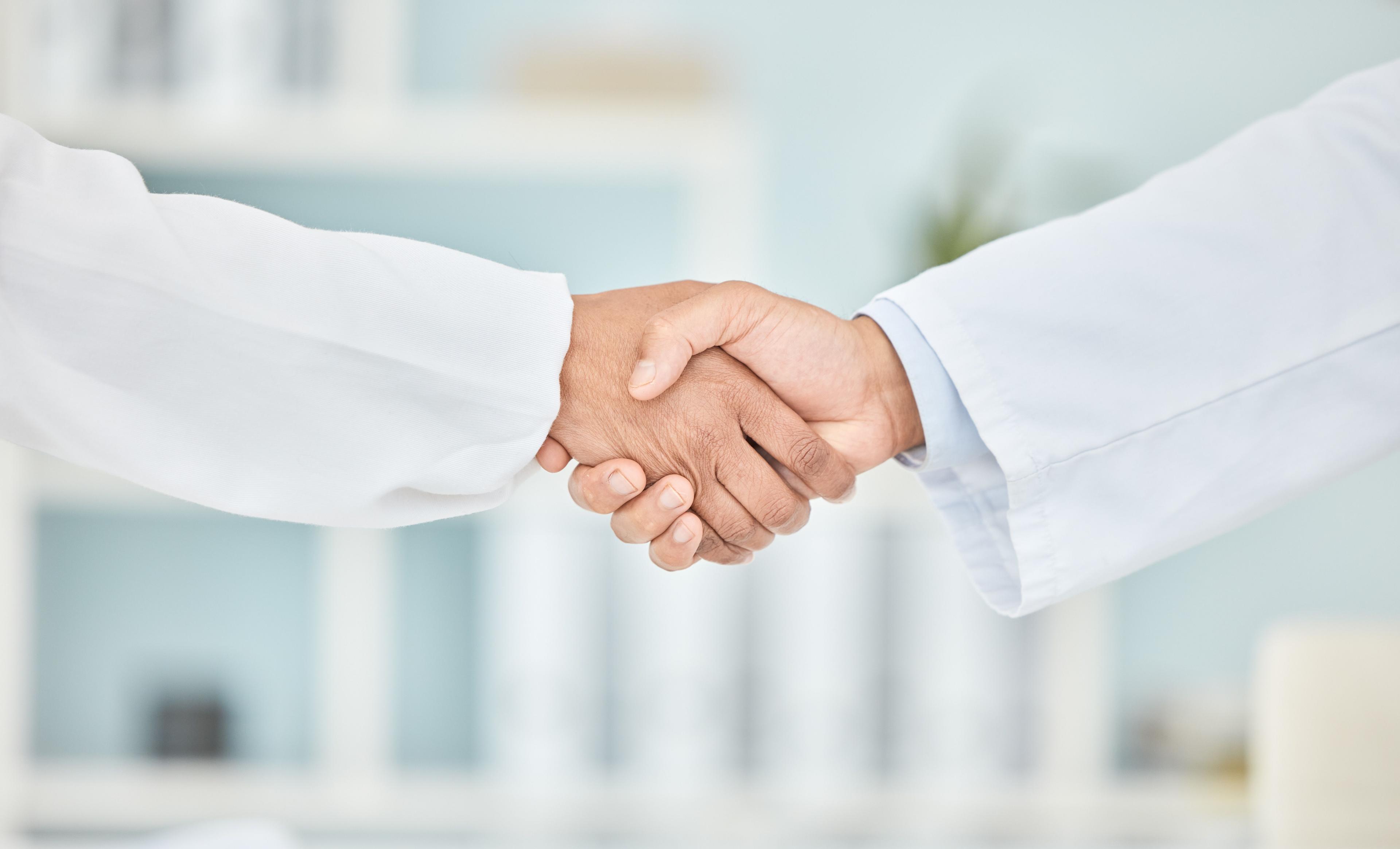 Two partnered physicians shaking hands, no faces visible.