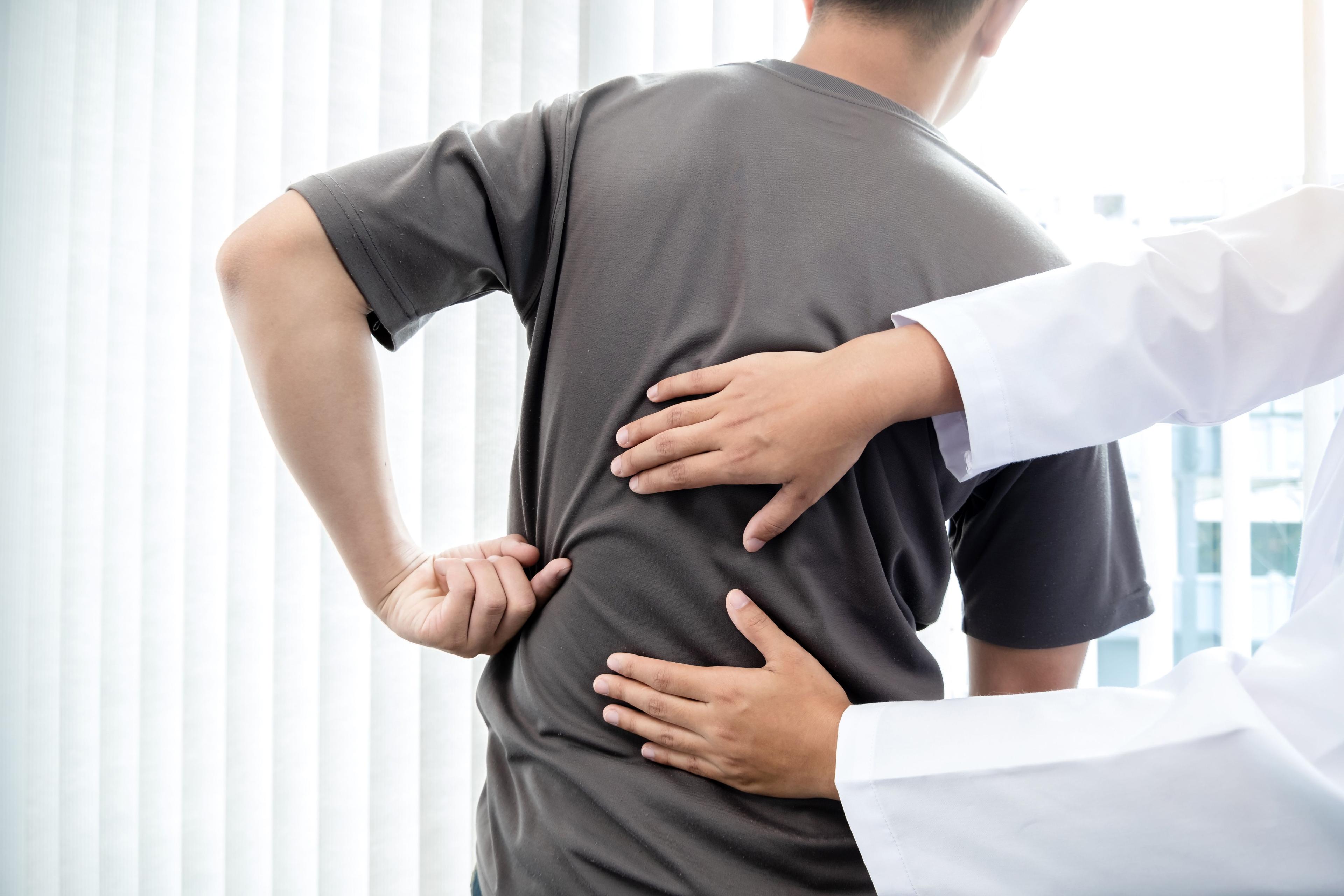 Therapist assisting patient with back pain post-surgery.