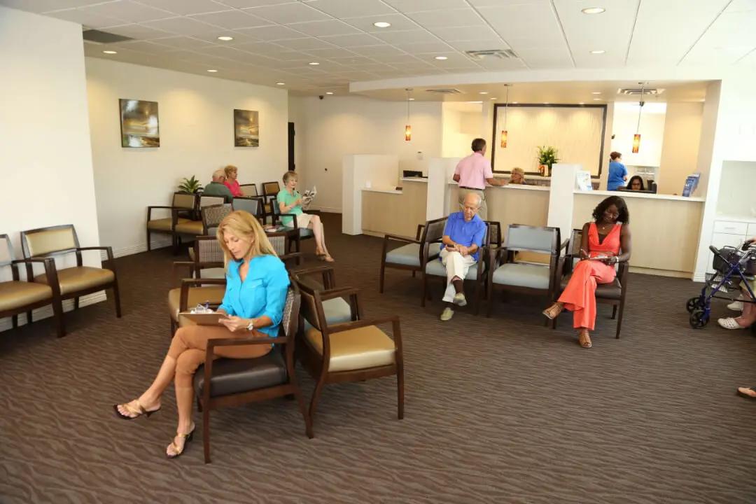 People sitting in a spacious, well-lit waiting room with a reception desk.