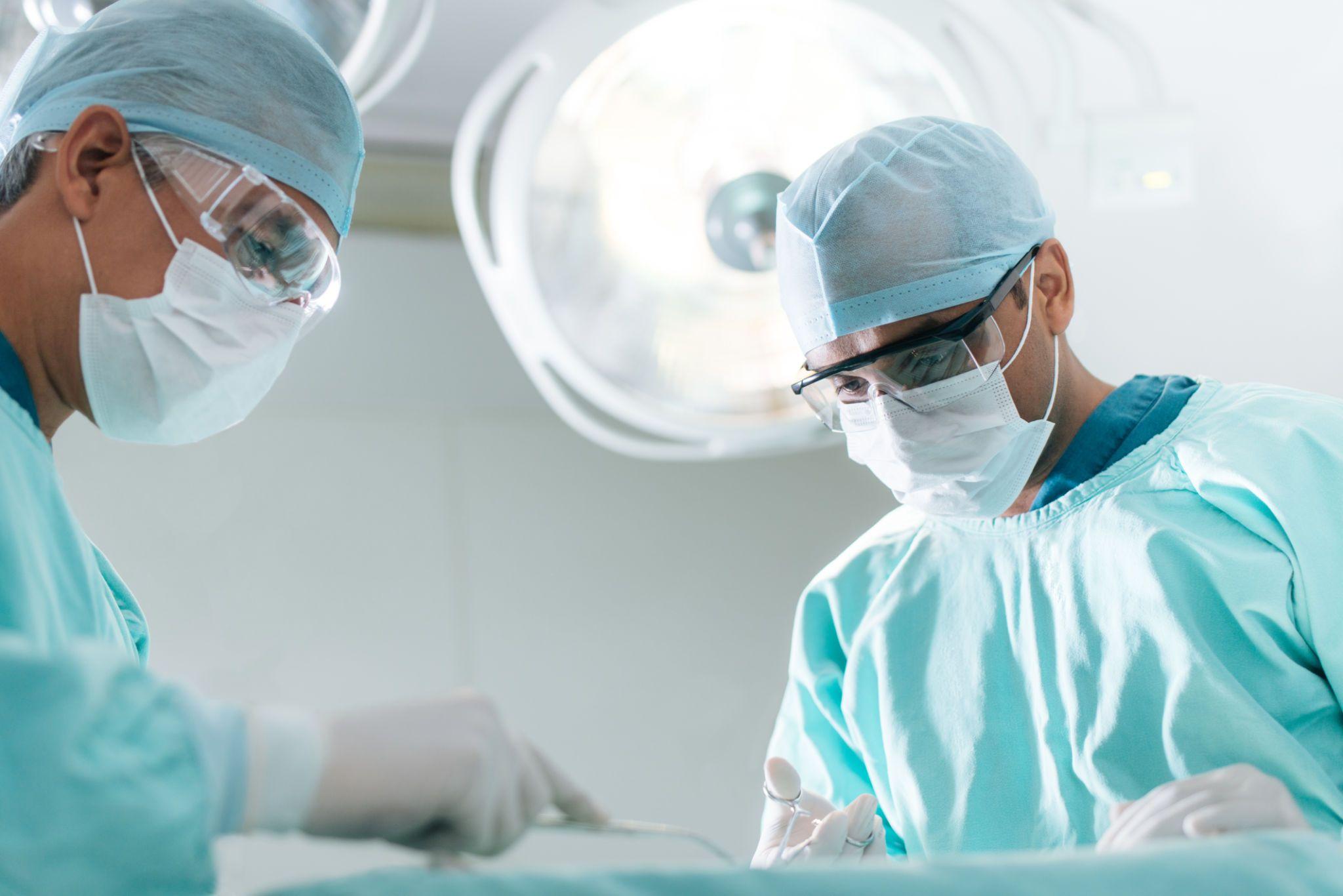 Two surgeons in scrubs and masks operating in a surgical room.