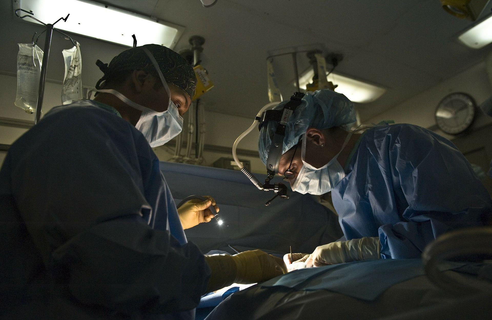 Two surgeons focus intently during a surgical procedure in a dimly lit operating room.
