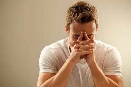 Man in white shirt looking stressed with hands covering face.