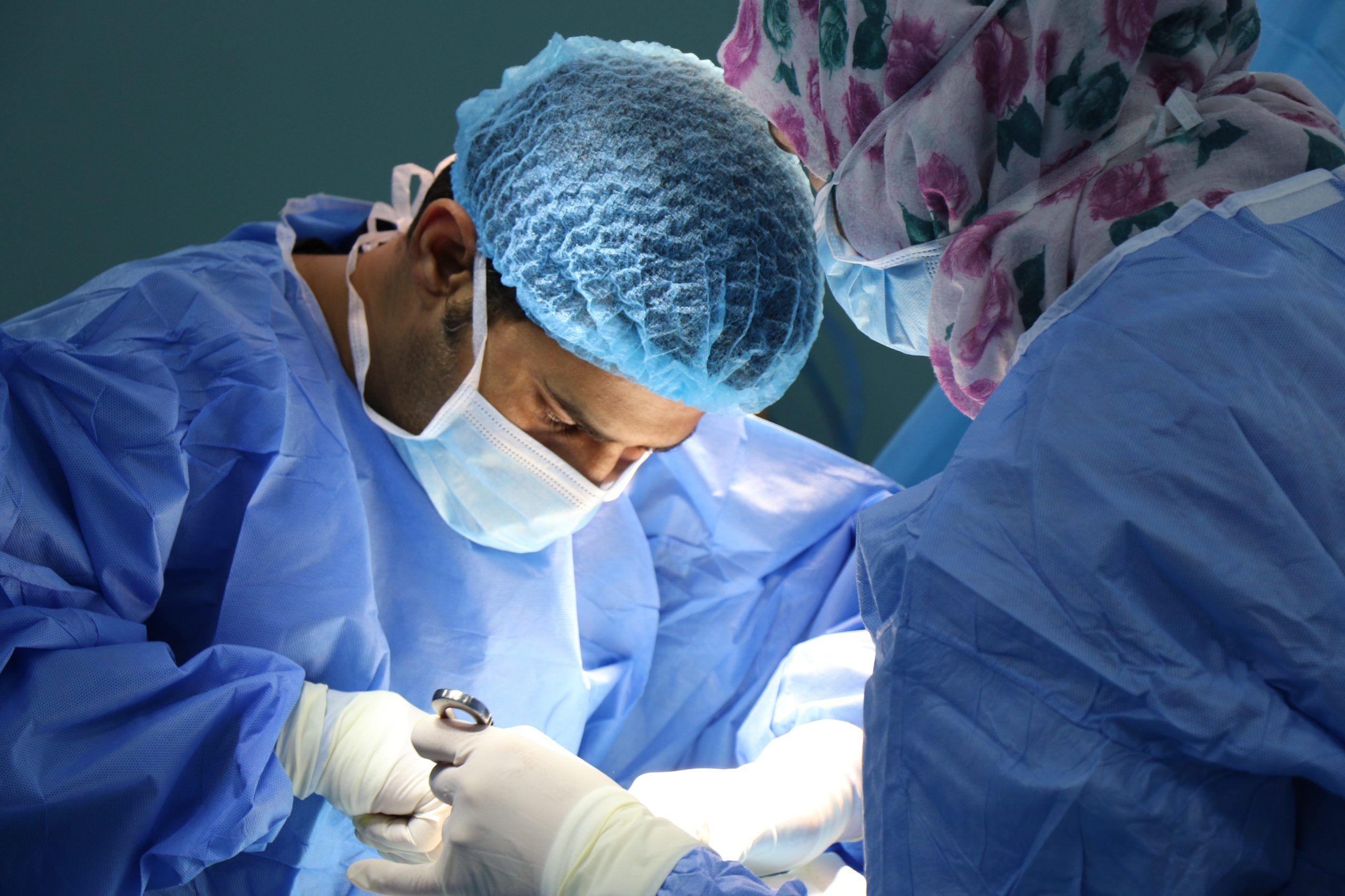 Surgeons in scrubs and masks performing a medical procedure.
