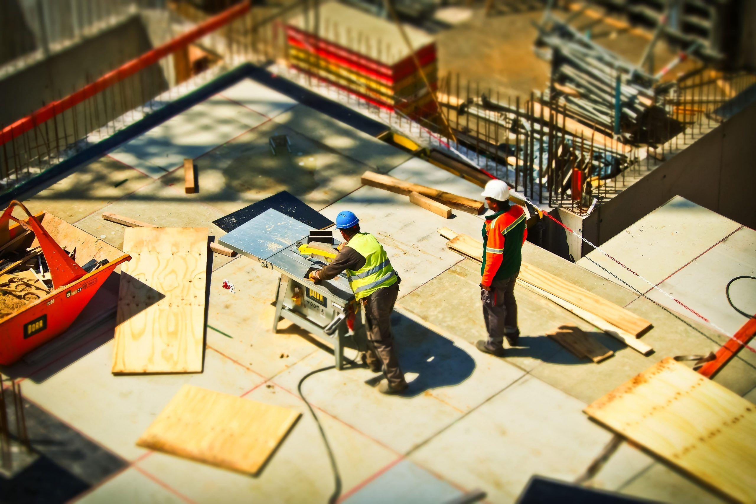 Two construction workers using a table saw at a busy construction site