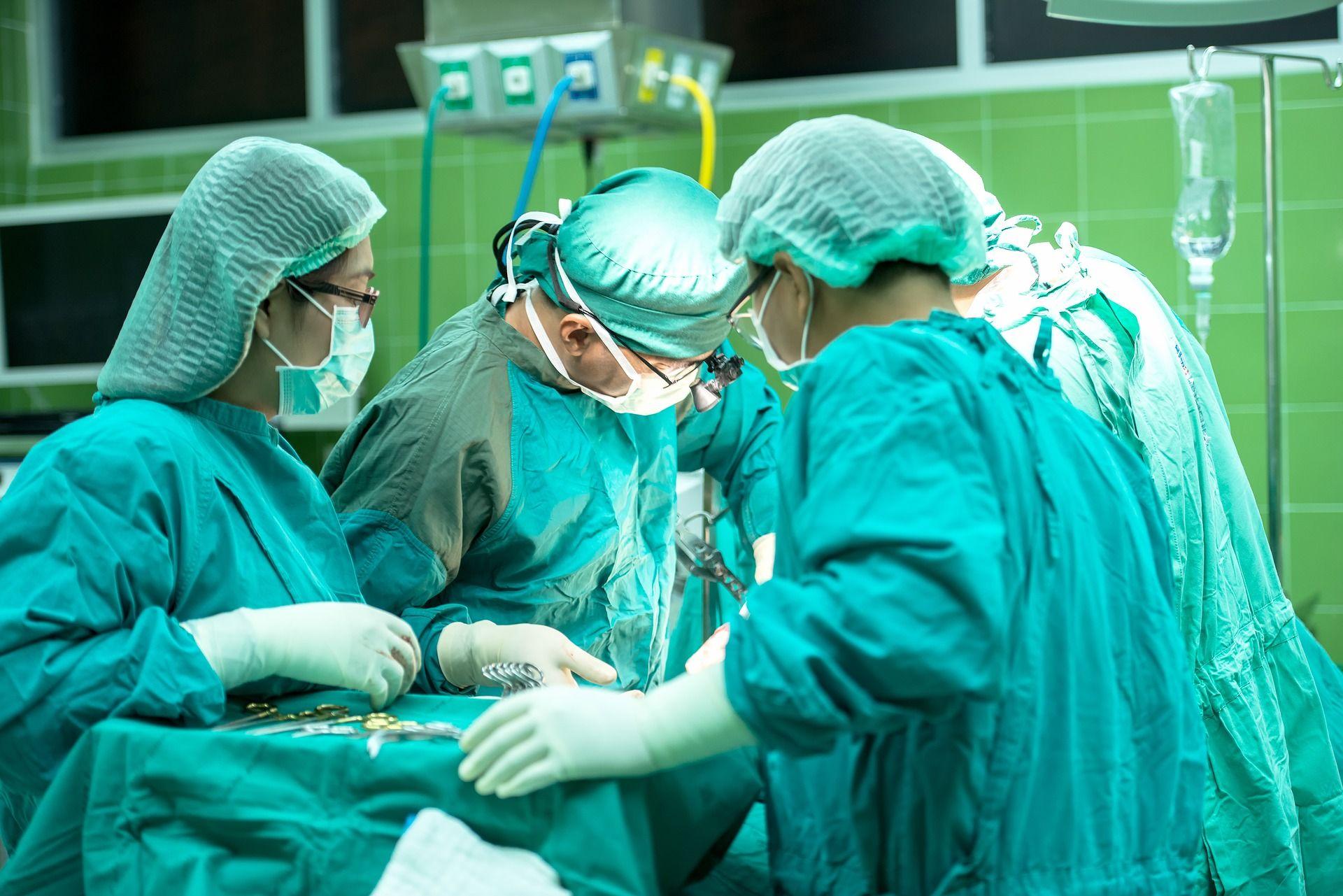 Four surgeons in scrubs operating in a green-tiled surgery room.