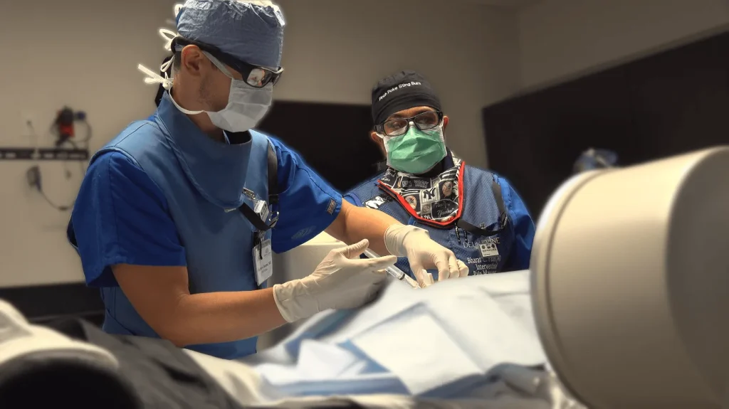 Two surgeons in scrubs and masks perform a procedure in an operating room.