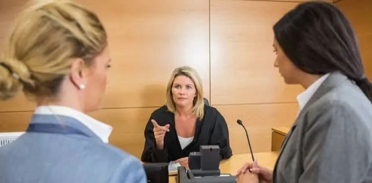 Three women discussing in a court setting, one acting as judge and two as lawyers.