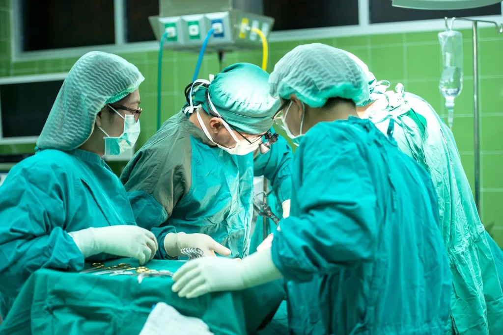 Four surgeons in scrubs operating in a green-tiled surgery room.