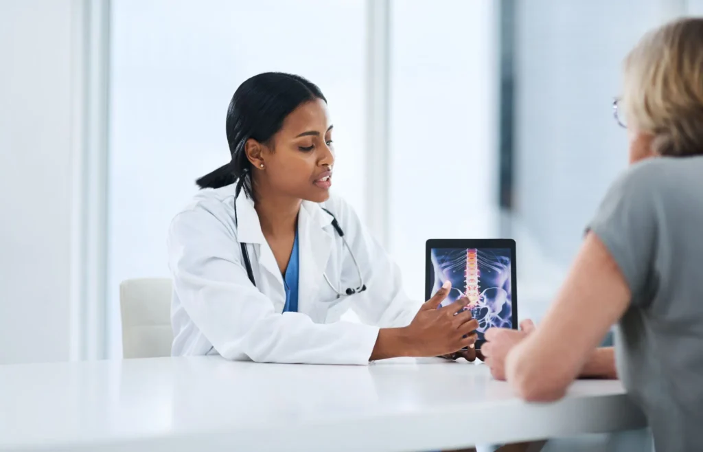 Doctor showing a patient spine X-ray on a tablet during a consultation.