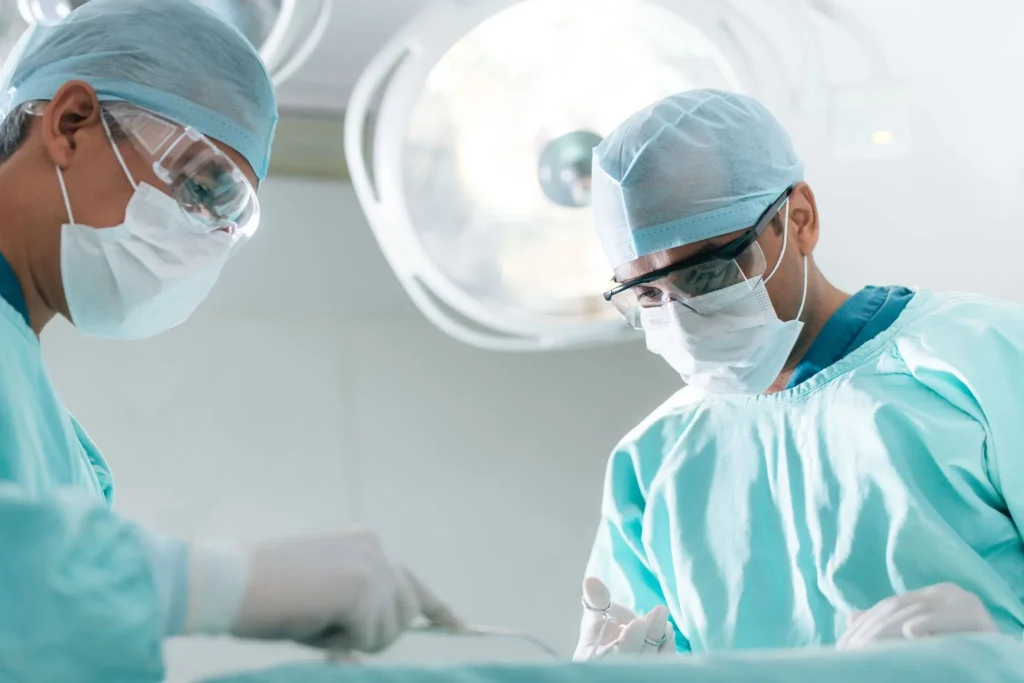 Two surgeons in scrubs and masks operating in a surgical room.