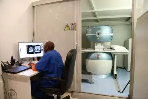A medical professional analyzes MRI scans at a computer beside an MRI machine.