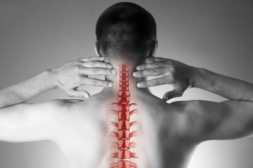 Man with hands on neck, highlighting a red spine illustration on his back.