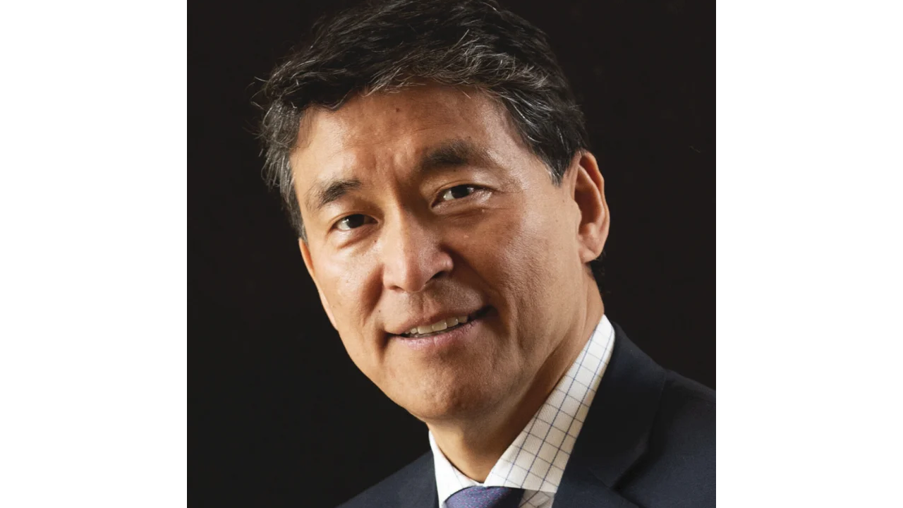 Smiling man in a suit with a dark background.
