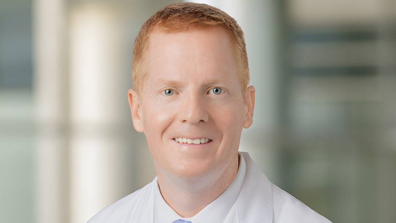 Smiling person in a white coat against a blurred background.