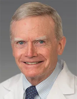 Elderly male doctor in white coat smiling at the camera.