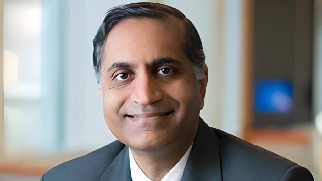 Smiling person in a suit with a blurred indoor background.