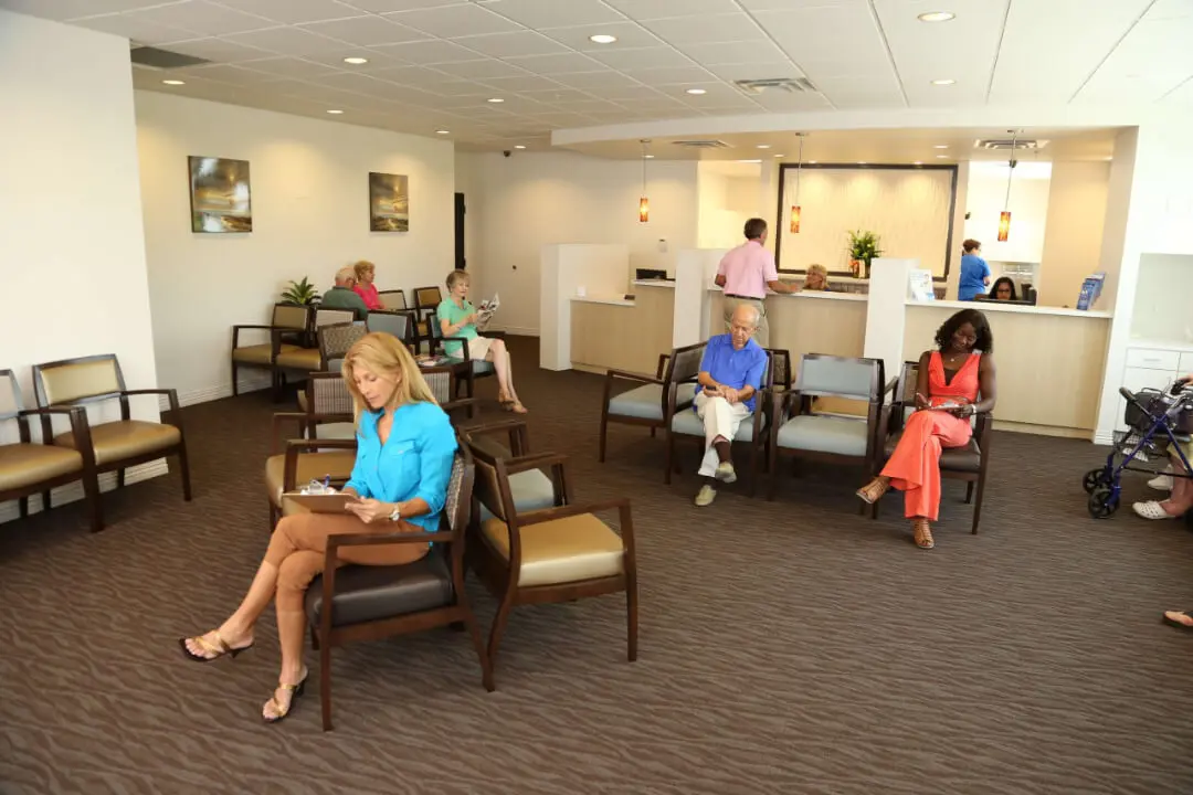 People sitting in a spacious, well-lit waiting room with a reception desk.