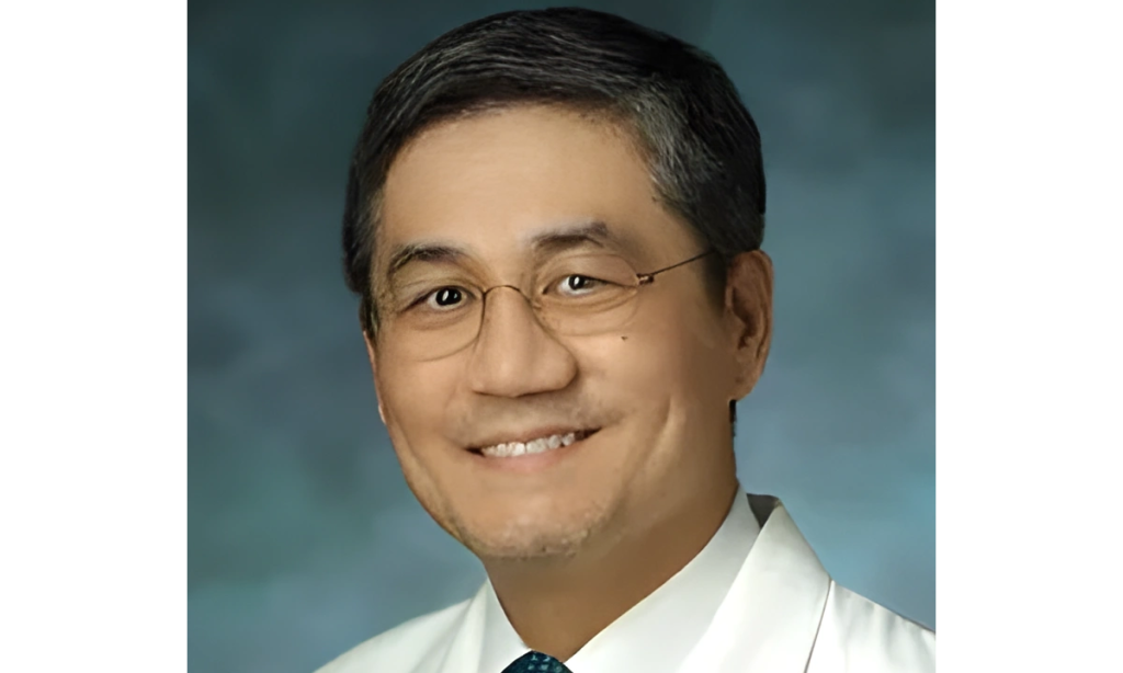 Smiling man in glasses and a white coat against a blue background.
