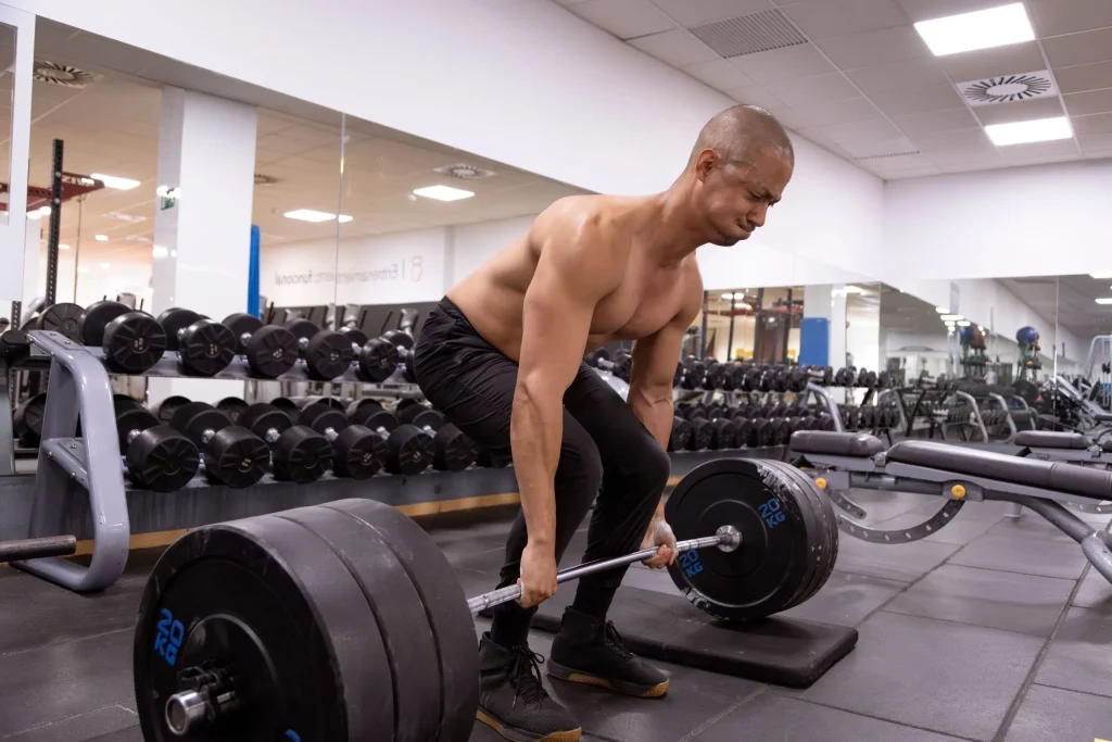 A man improperly lifting a heavy barbell in a gym, risking a herniated disc.