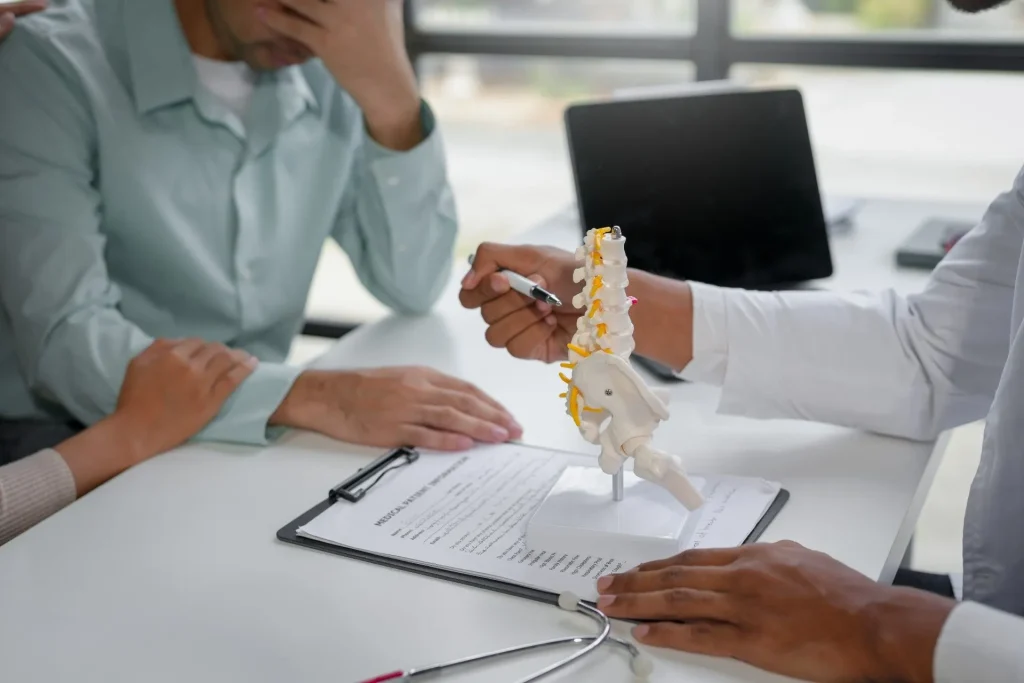 A doctor explains a spine model to a concerned worker regarding compensation paperwork.