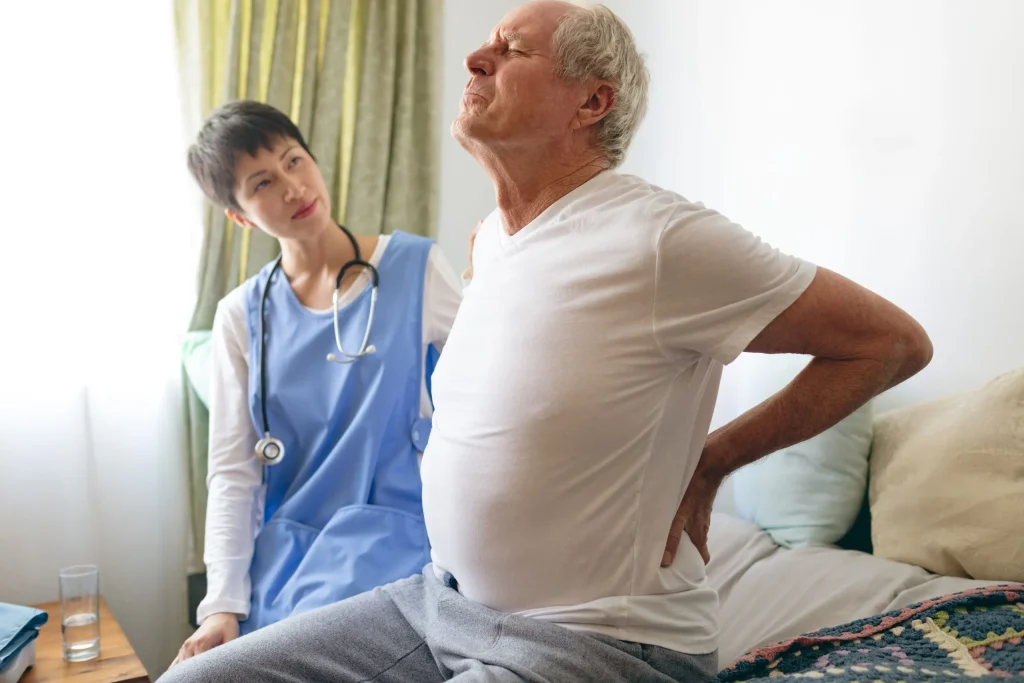 A nurse assists an elderly man experiencing back pain, highlighting the role of nurses in spine surgery and recovery care.