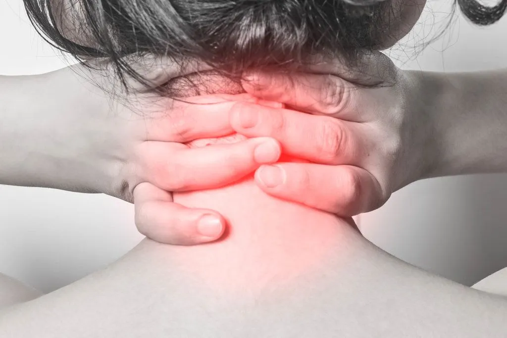  person experiencing neck pain, clutching the back of their neck with both hands, highlighting the area with visible red inflammation.