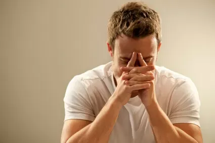Man in white shirt looking stressed with hands covering face.