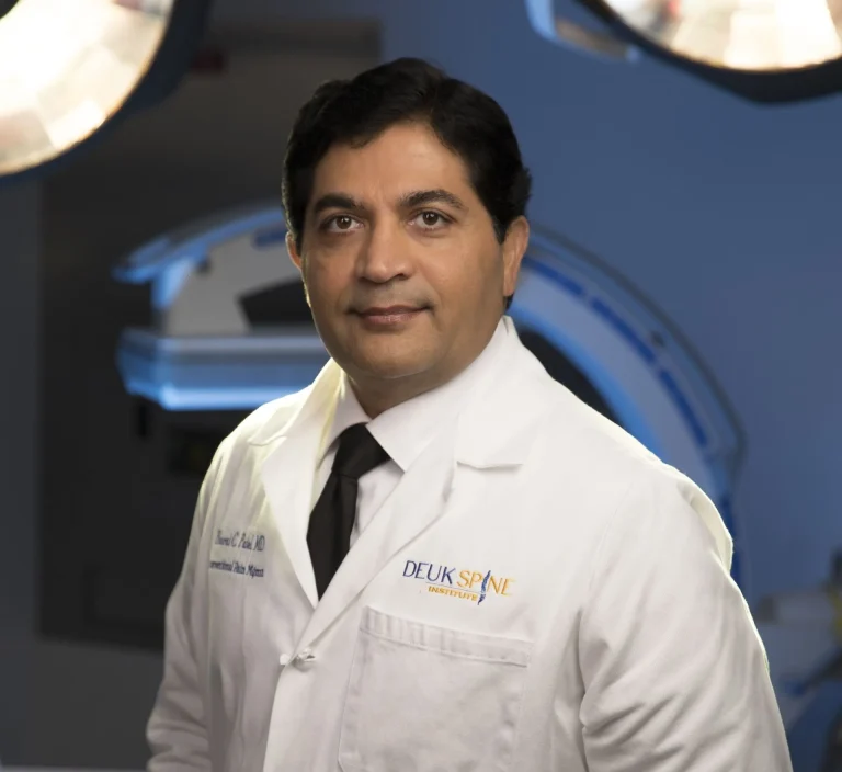 A man in a white lab coat stands in a medical setting.