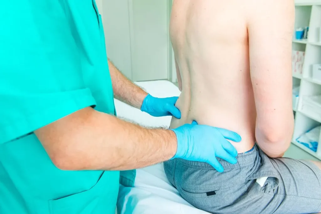 Patient sitting on table having his back examined by a doctor.