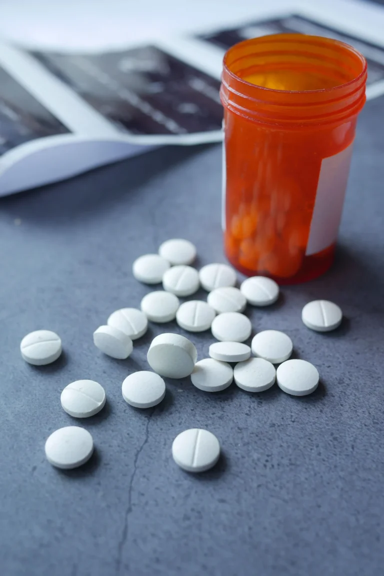 White pills scattered near an open orange pill bottle on a gray surface.