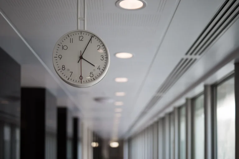 A round clock showing 10:10 hangs from a ceiling in a modern hallway.