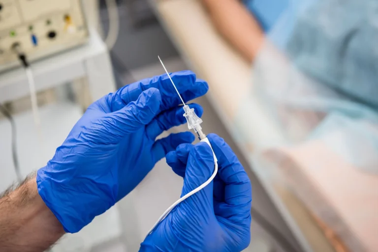 Gloved hands prepare a medical needle for insertion.