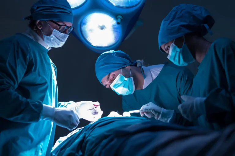 Three surgeons in masks performing surgery under bright lights.