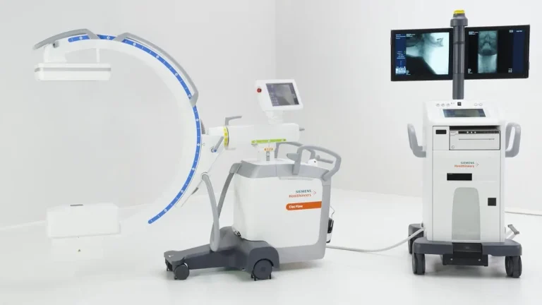 A Siemens Healthineers C-arm X-ray machine with two monitors displaying medical images.
