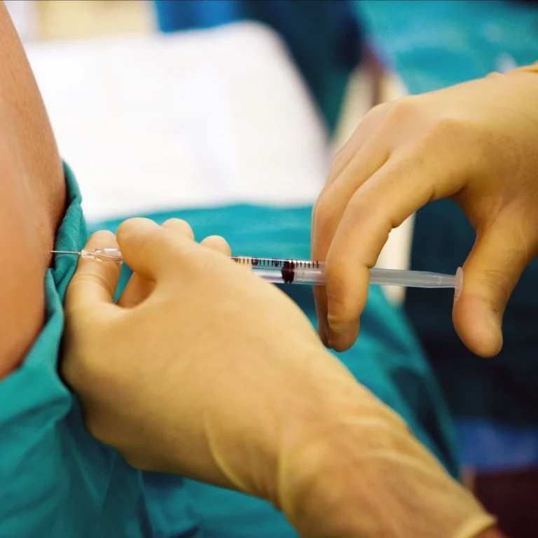 Gloved hands administering an injection into a patient's arm.