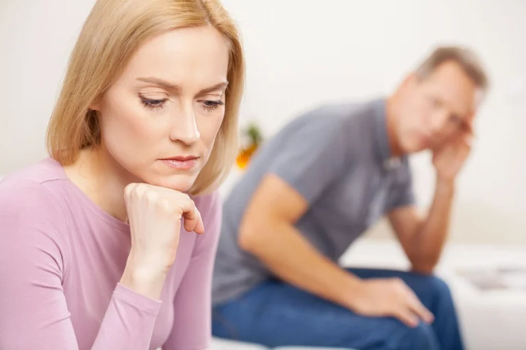 A woman appears upset in the foreground while a man is blurred in the background.