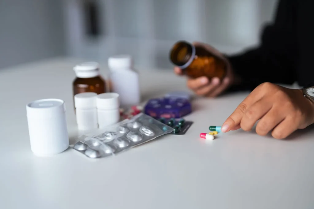Person selecting pills from a variety of medicine bottles on a table.