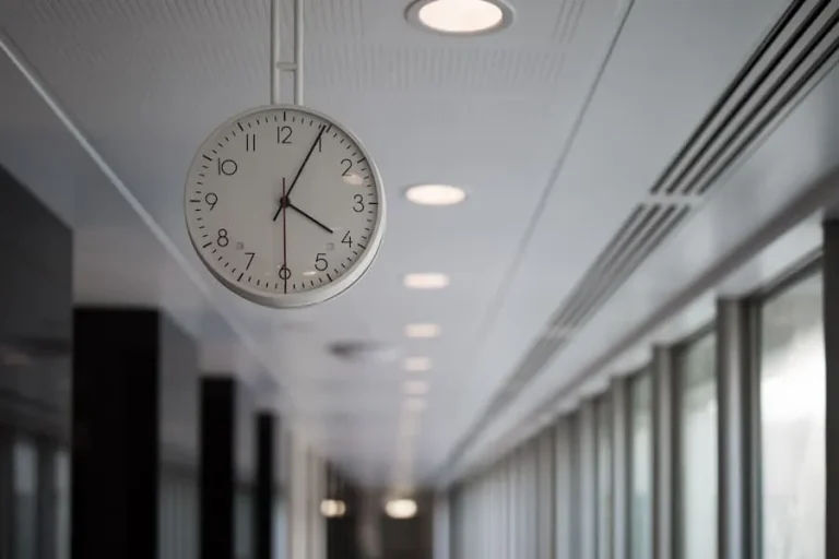 A round wall clock showing 2:06 hangs in a well-lit corridor.