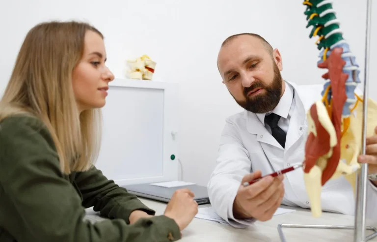 A doctor explains a spine model to a patient in an office setting.