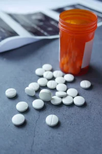 White pills scattered next to an open orange prescription bottle.