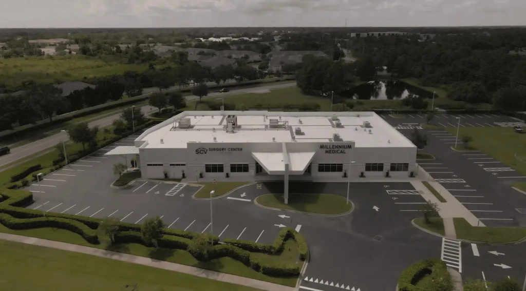 Aerial view of a white building labeled SCV Surgery Center and Millennium Medical, surrounded by parking lots and greenery.