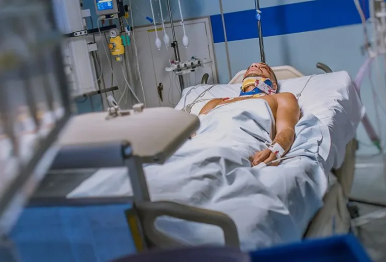 A patient with a neck brace lies in a hospital bed, surrounded by medical equipment.