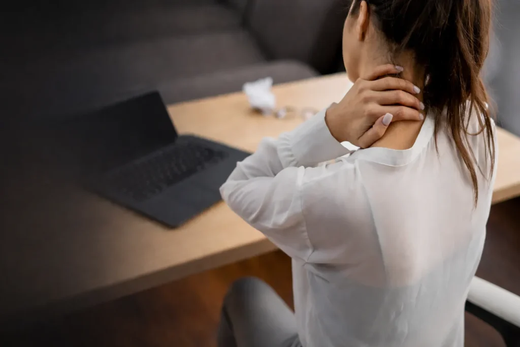 Person sitting at a desk massaging their neck near a laptop.