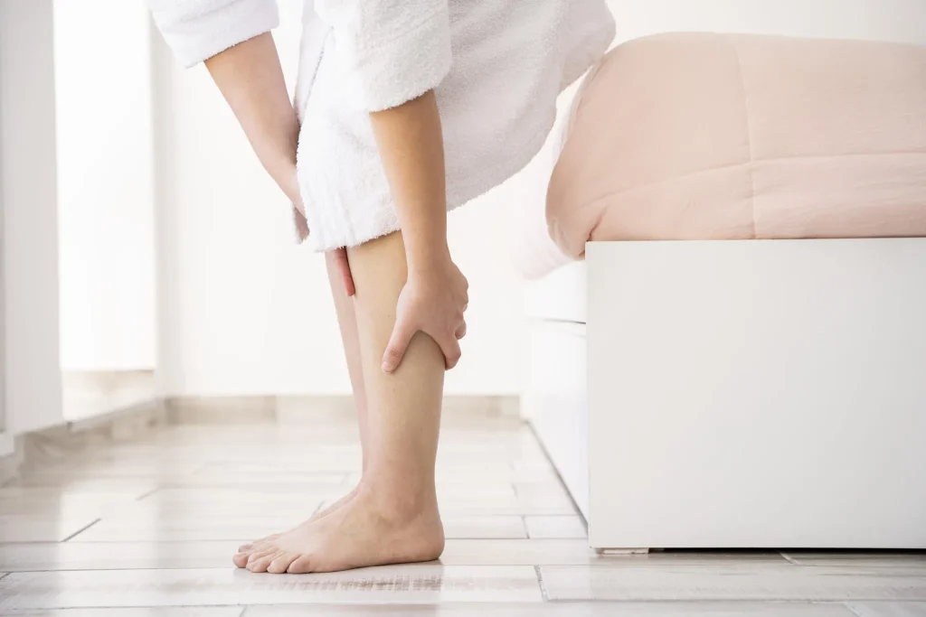 Person in a white bathrobe holding their calf near a bed.