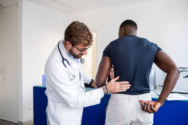 A doctor examines a patient's lower back in a medical office.