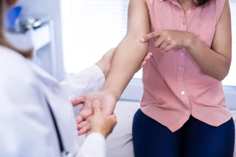 A doctor examines a patient's arm while the patient points to a spot.